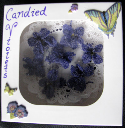 candied_violets Candied violets in a hand-labeled box, stuck to a dainty paper doily, with butterfly and violet sparkly stickers that also look sugared decorating the box