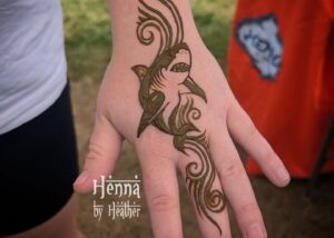 Shark henna tattoo for boys and girls, women and men - showing a simple but well-executed realistic shark centerpiece and abstract swirly water wave designs in a 90s "tribal" style going up the wrist and down the finger